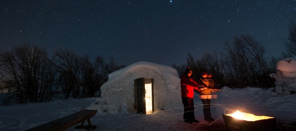 A couple in a snow igloo by a fire