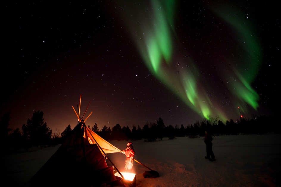 People near a kota and fire amid the Northern Lights