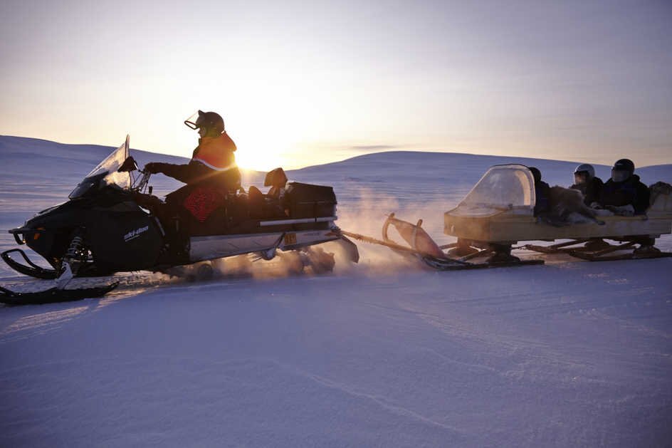 A snowmobile pulling a group of travellers