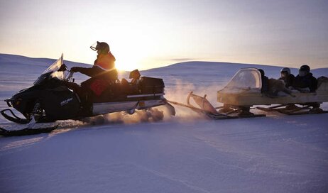 A snowmobile pulling a group of travellers