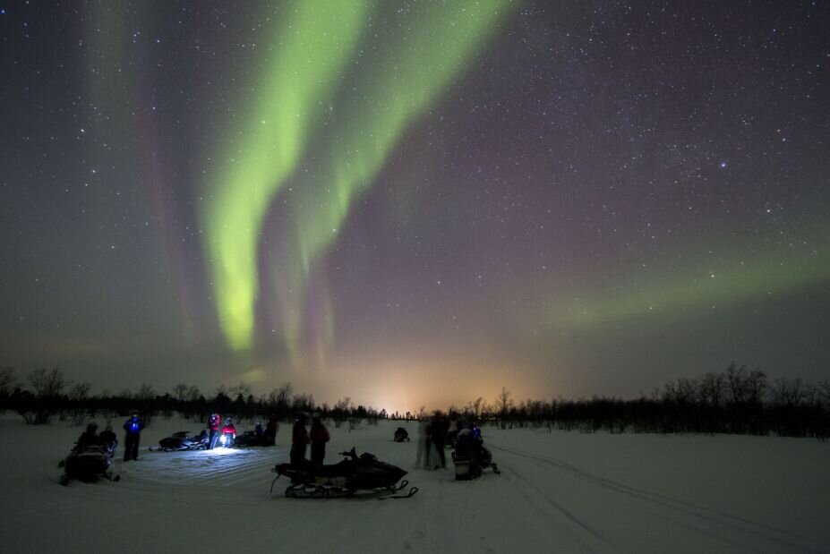 A group of adventurers on snowmobile admiring the Northern Lights
