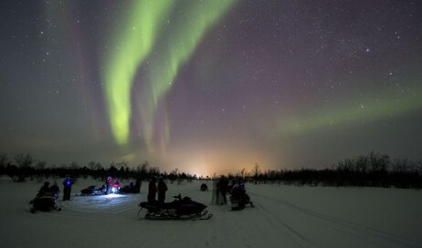 A group of adventurers on snowmobile admiring the Northern Lights