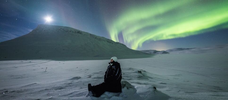 A woman admiring the Northern Lights near Saana Fell in Kilpisjarvi
