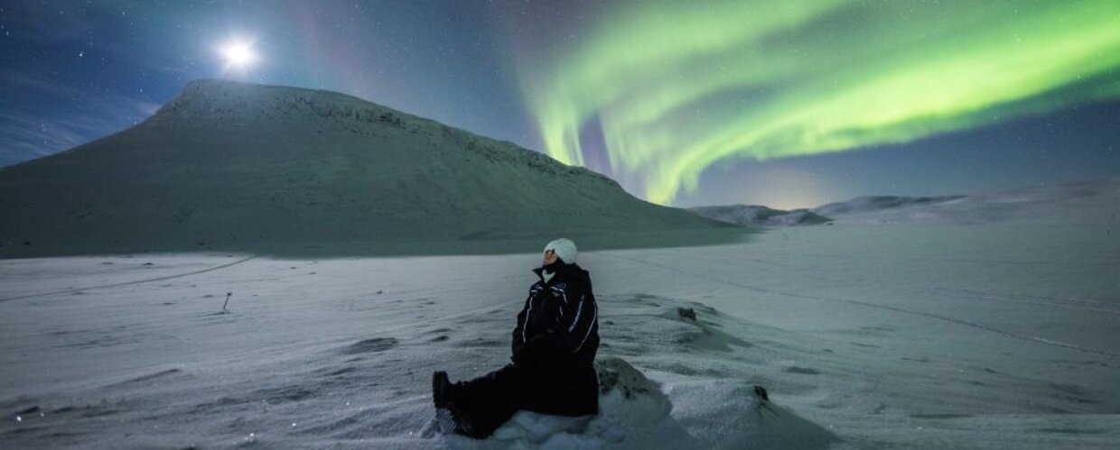A woman admiring the Northern Lights near Saana Fell in Kilpisjarvi