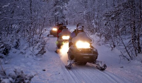 A line of adventurers driving snowmobiles
