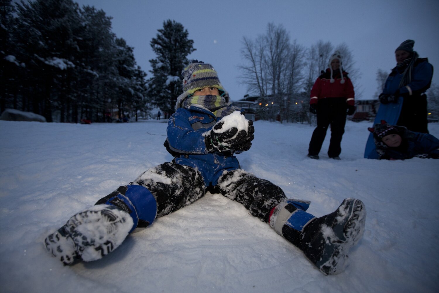 A boy makes a snowball and frolics in the snow