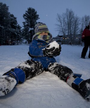 A boy makes a snowball and frolics in the snow