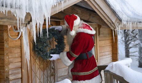 Santa hanging a wreath on his cabin