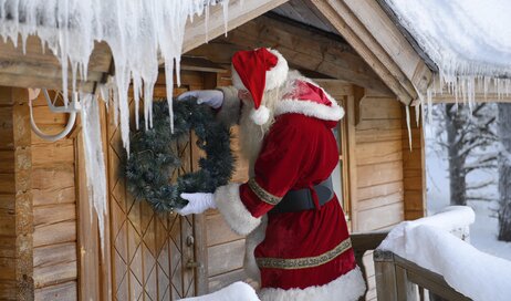 Santa hanging a wreath on his cabin