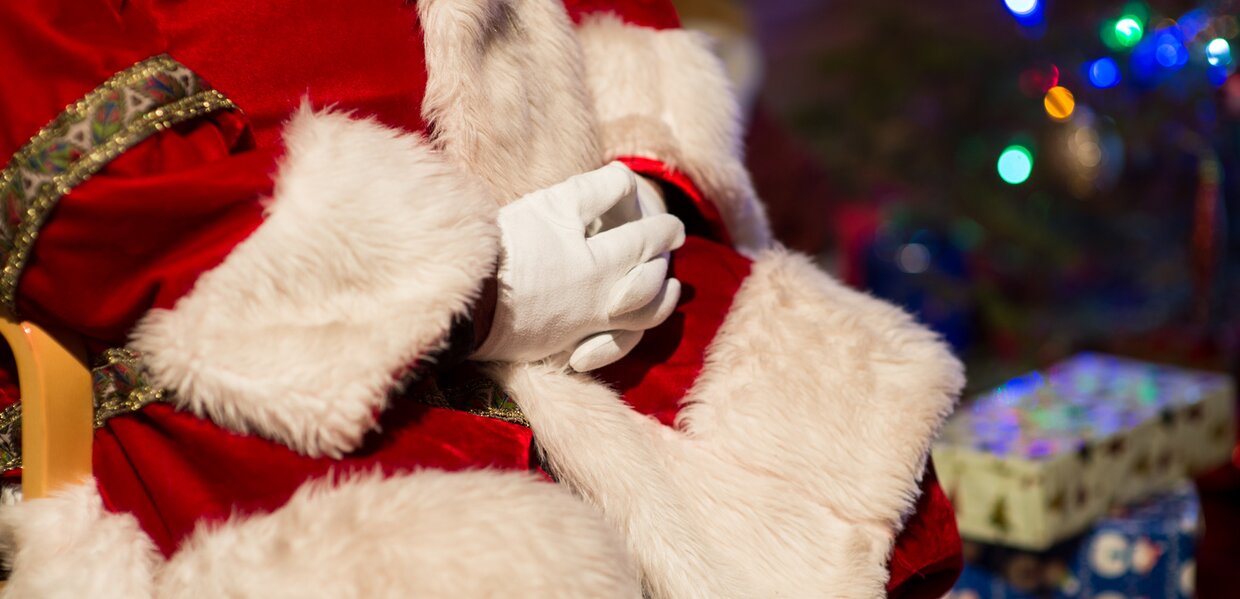 Santa with arms folded by a Christmas tree
