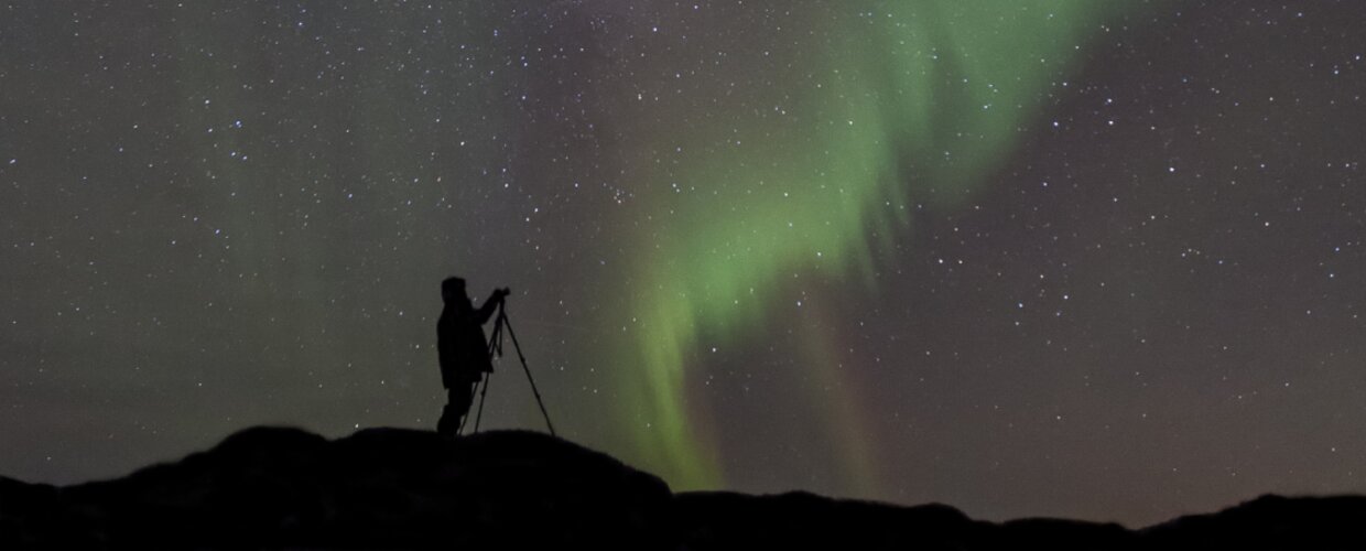 A man taking a photo on his camera of the Northern Lights