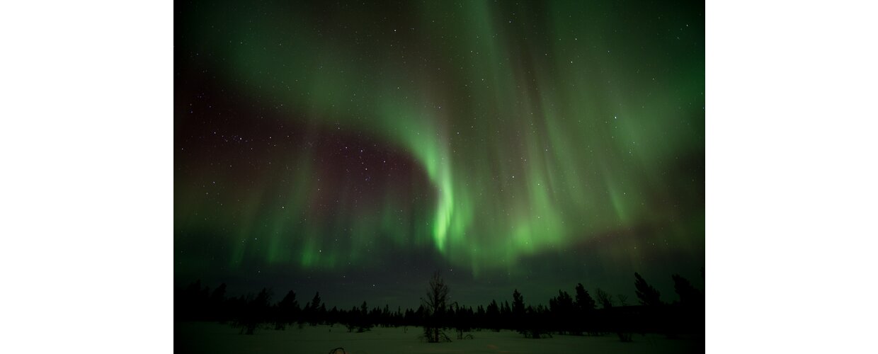 A quiet, snow-covered landscape with the Northern Lights swirling overhead