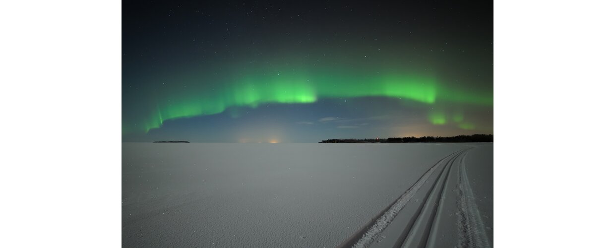 Ski tracks across a vast horizon of snow with the Northern Lights shimmering above